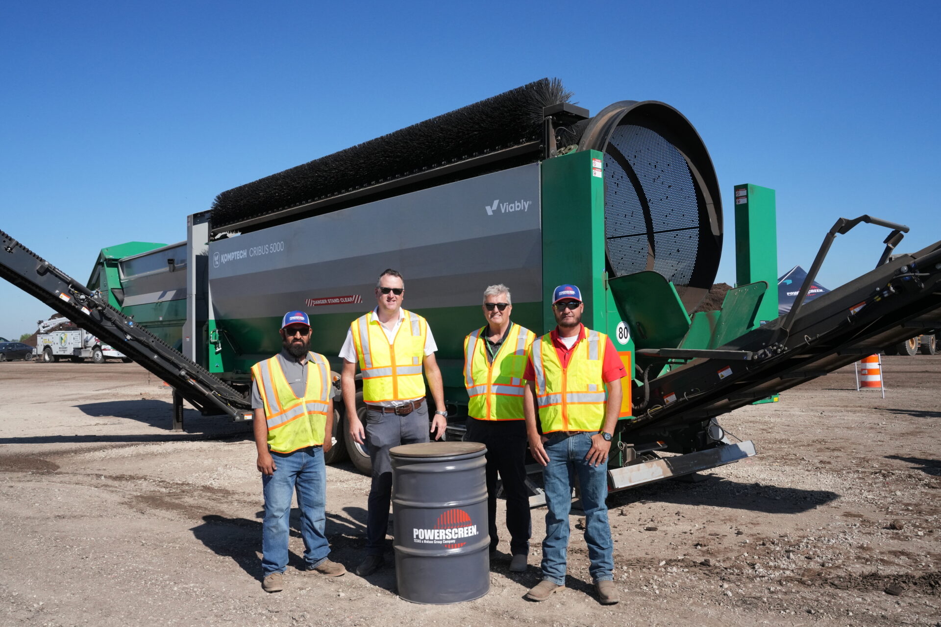 Four men standing in front of a Komptech trommel screen machine at a demo day for a compost summit event